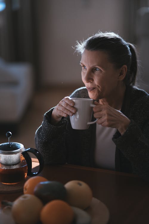A person sitting thoughtfully at a table with a cup of tea, warm morning light